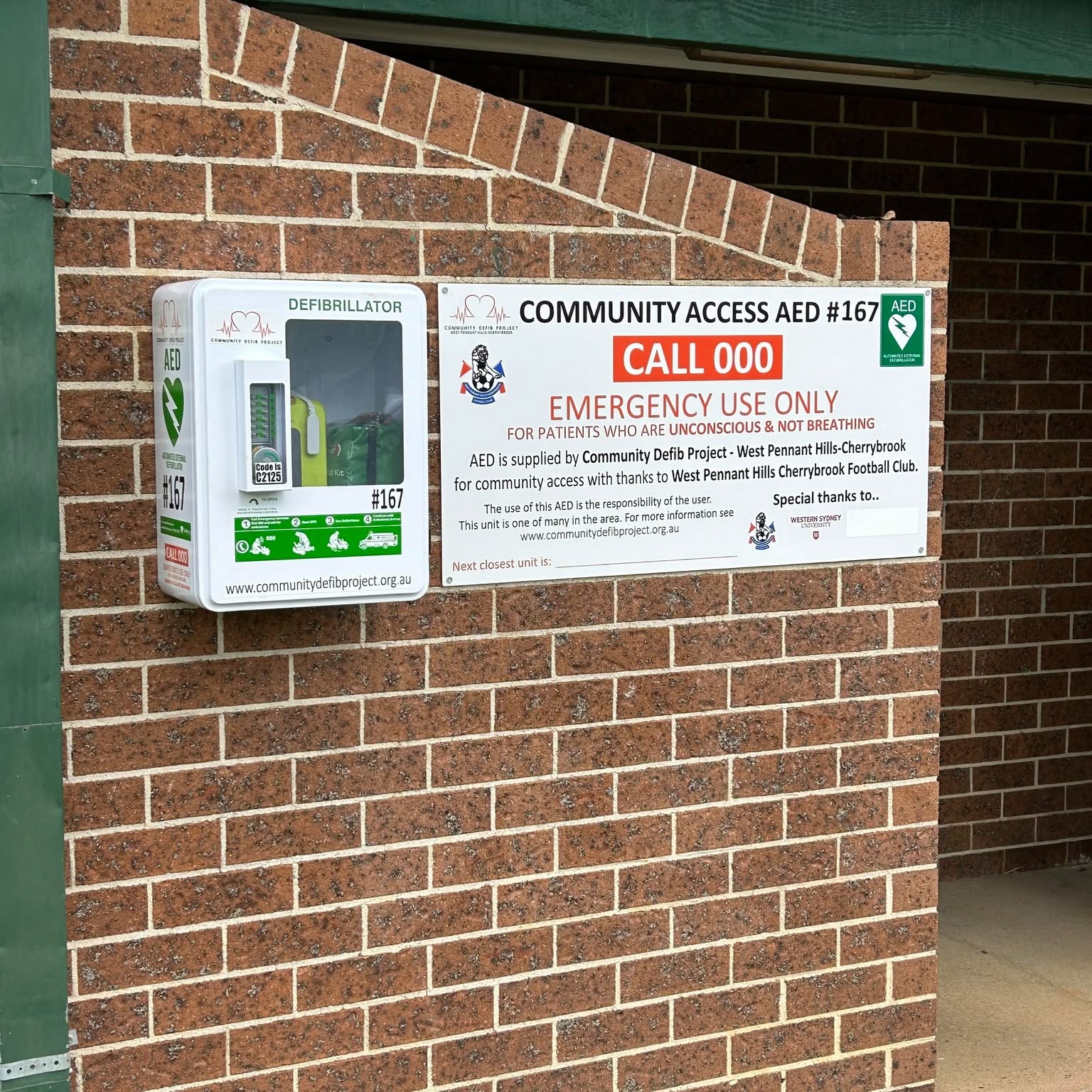 Community AED 167 mounted beside its emergency sign
